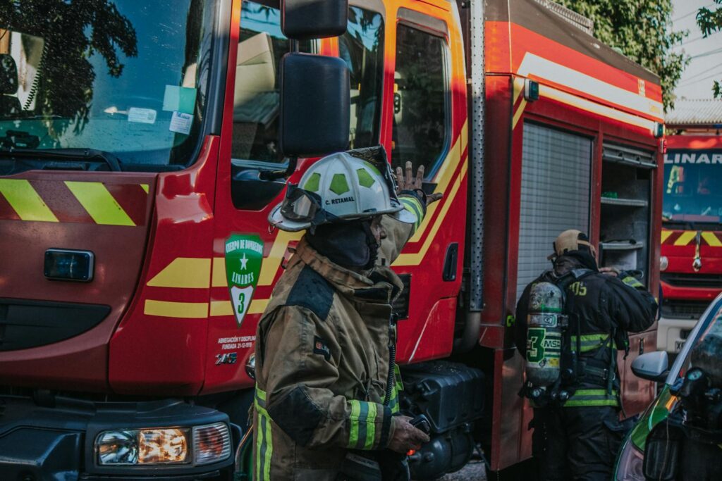 Firefighters in protective gear working near a red fire engine during a daytime emergency.