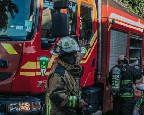Firefighters in protective gear working near a red fire engine during a daytime emergency.
