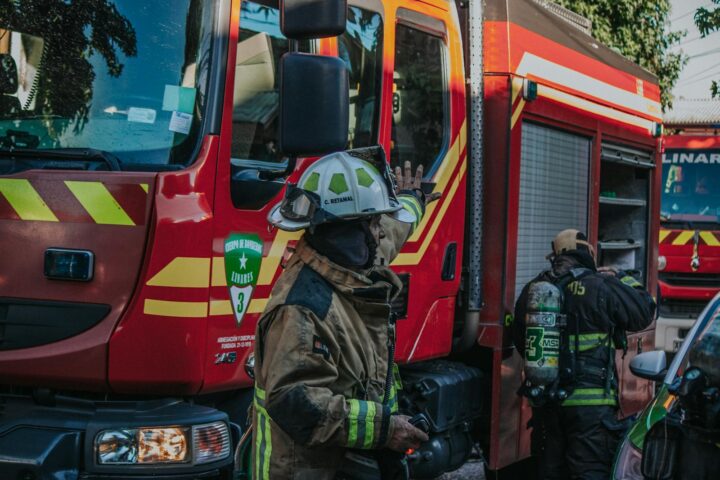 Firefighters in protective gear working near a red fire engine during a daytime emergency.