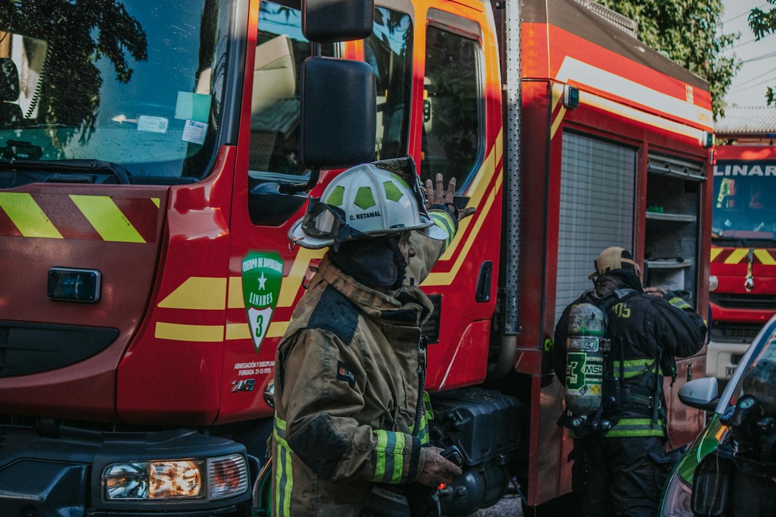 Firefighters in protective gear working near a red fire engine during a daytime emergency.